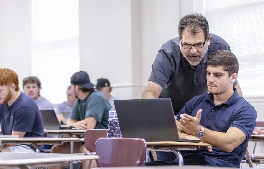 A professor engages with a student in the classroom