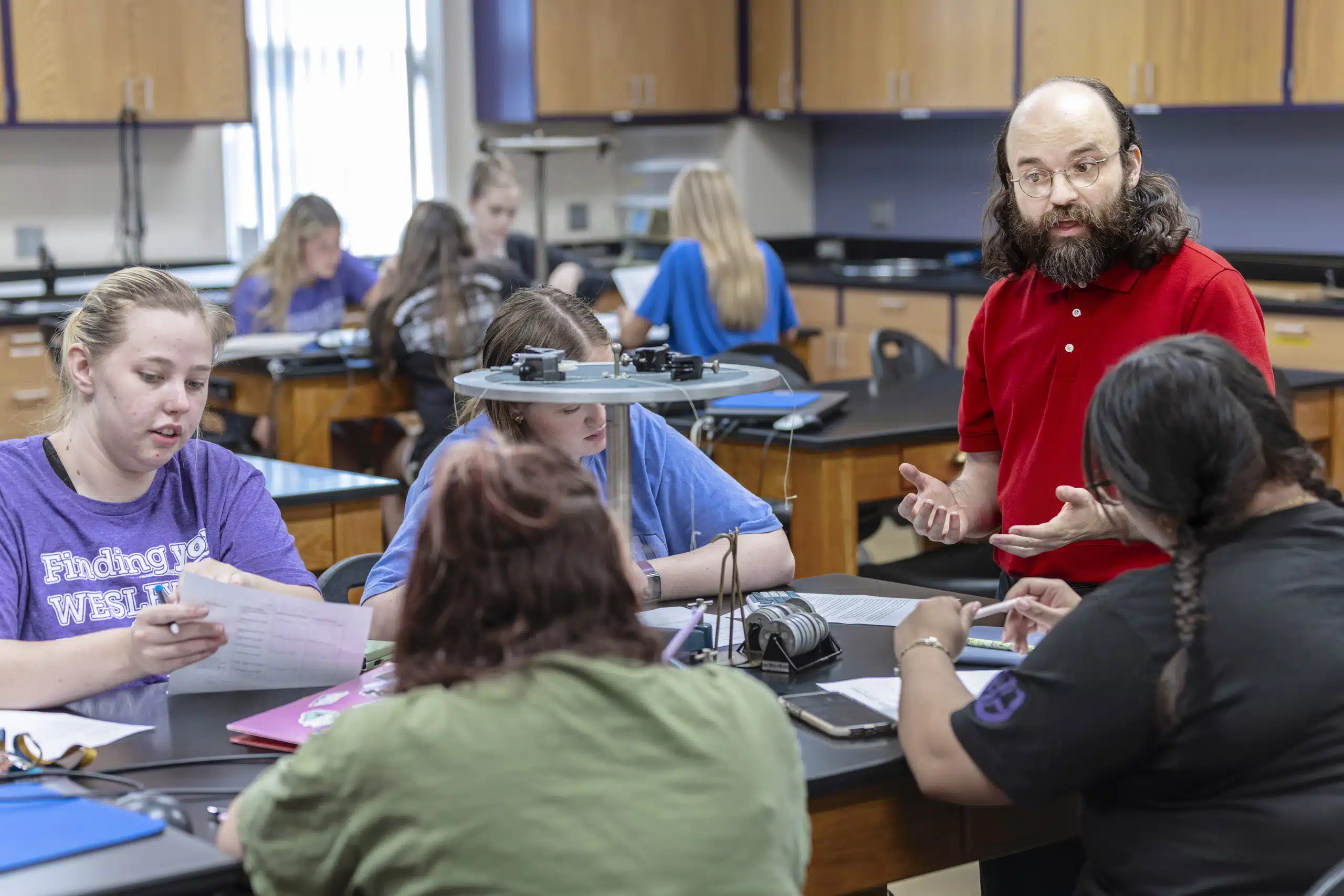 A professor engages with a group of students at a science lab table