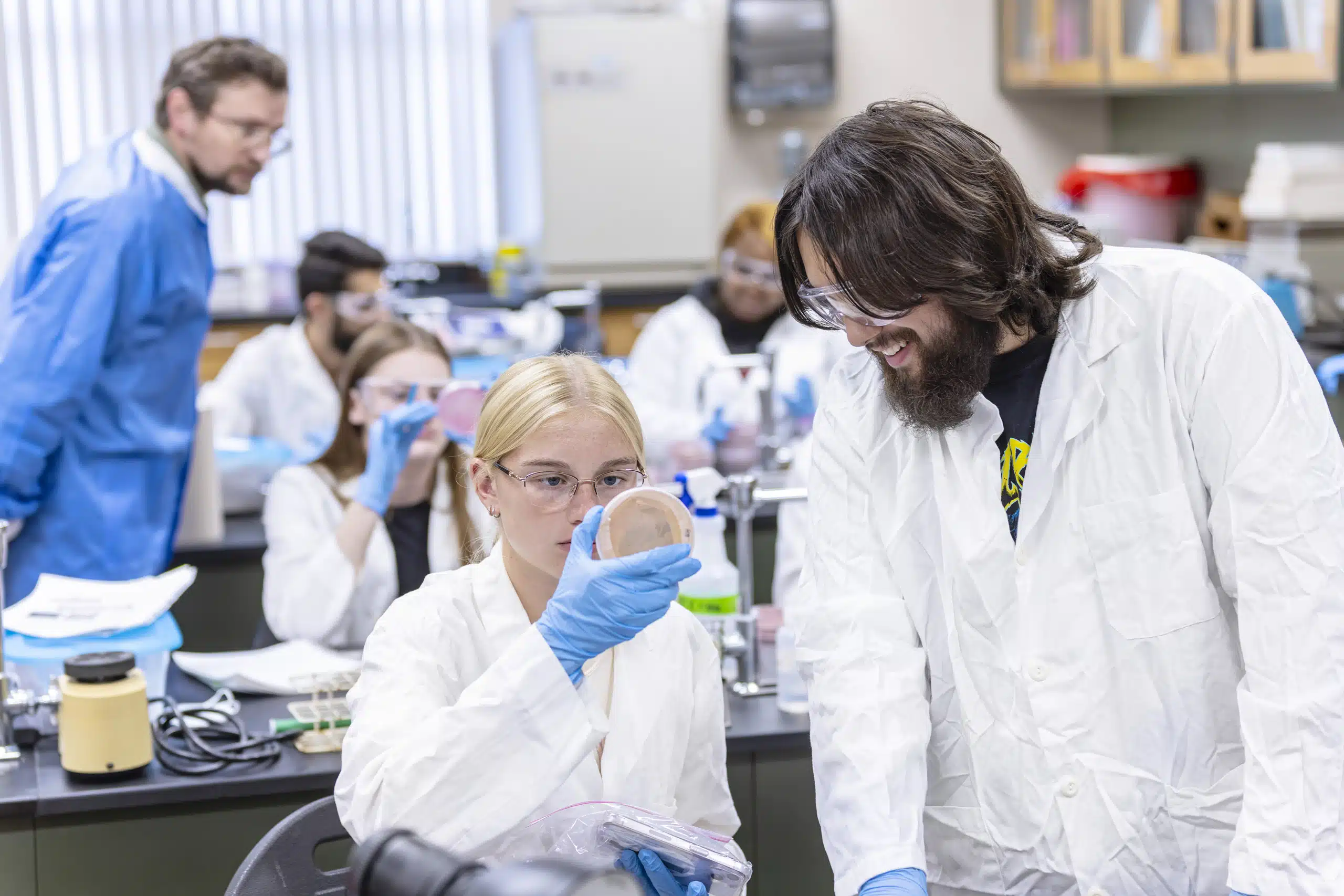 Students in white lab coats working and observing inside a KWC science lab