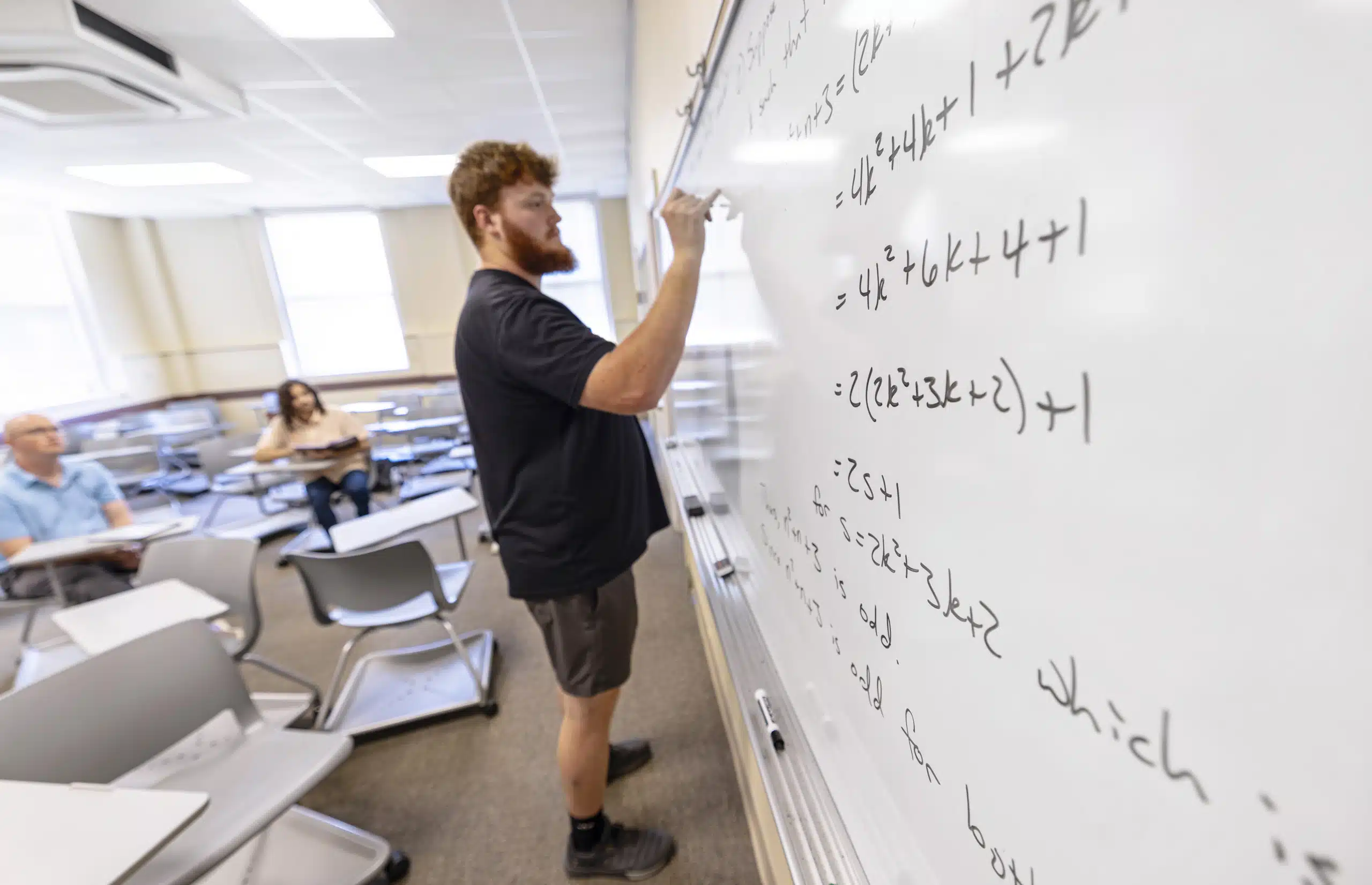 A student demonstrating an equation on a whiteboard inside a classroom