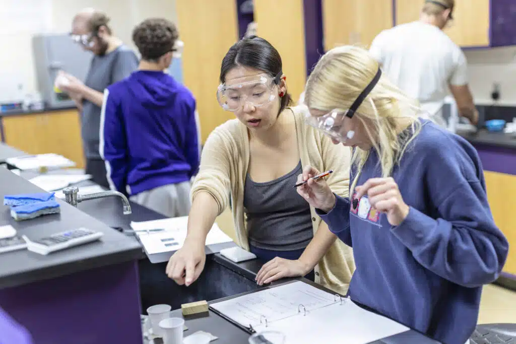 Two KWC students in safety googles working with a hands-on activity inside a KWC science lab