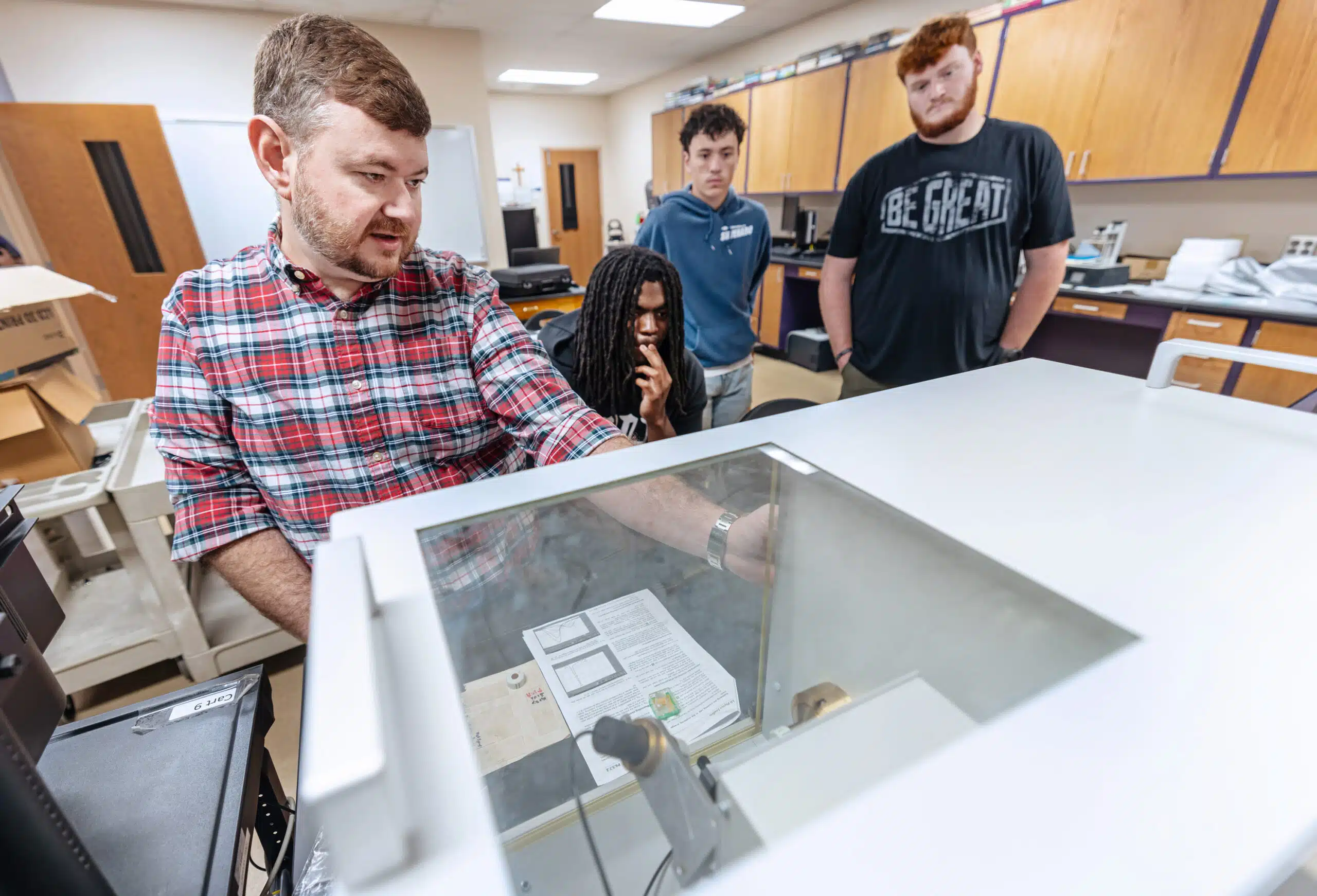students look over professors shoulder while using instrument