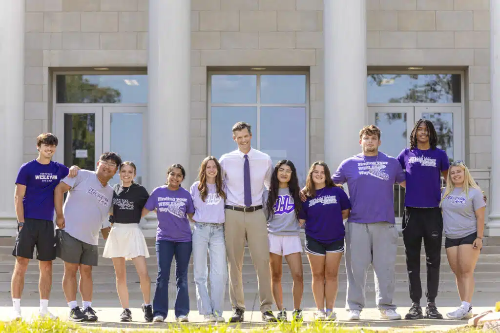 University President Dr. Cousins posing for a photo with a group of KWC students outside with large columns behind them