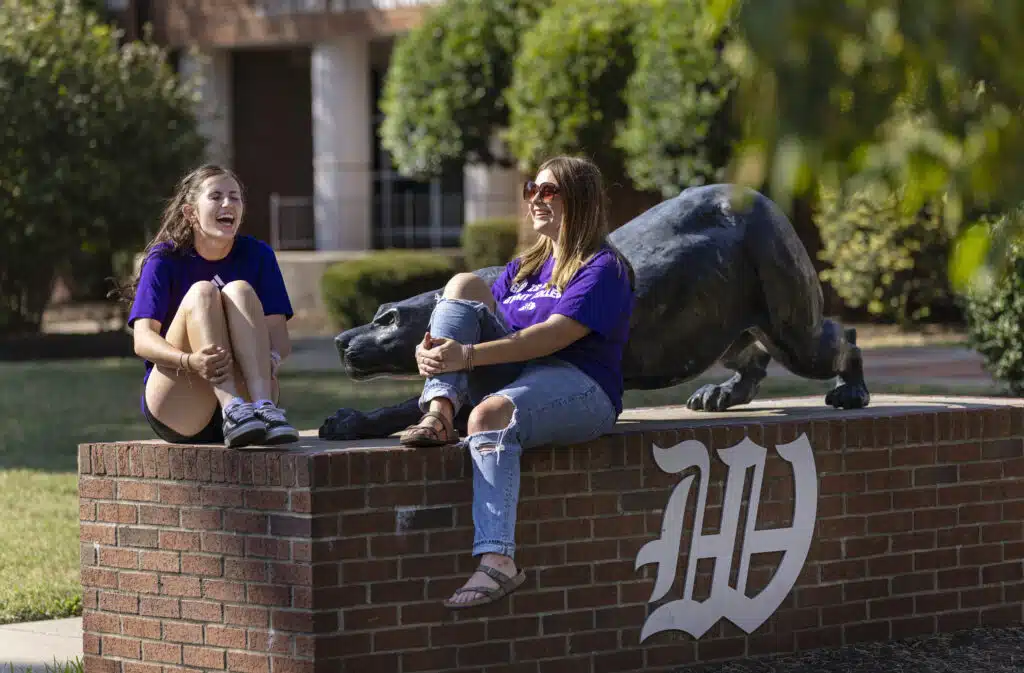 Two students sitting on the brick with the panther statue