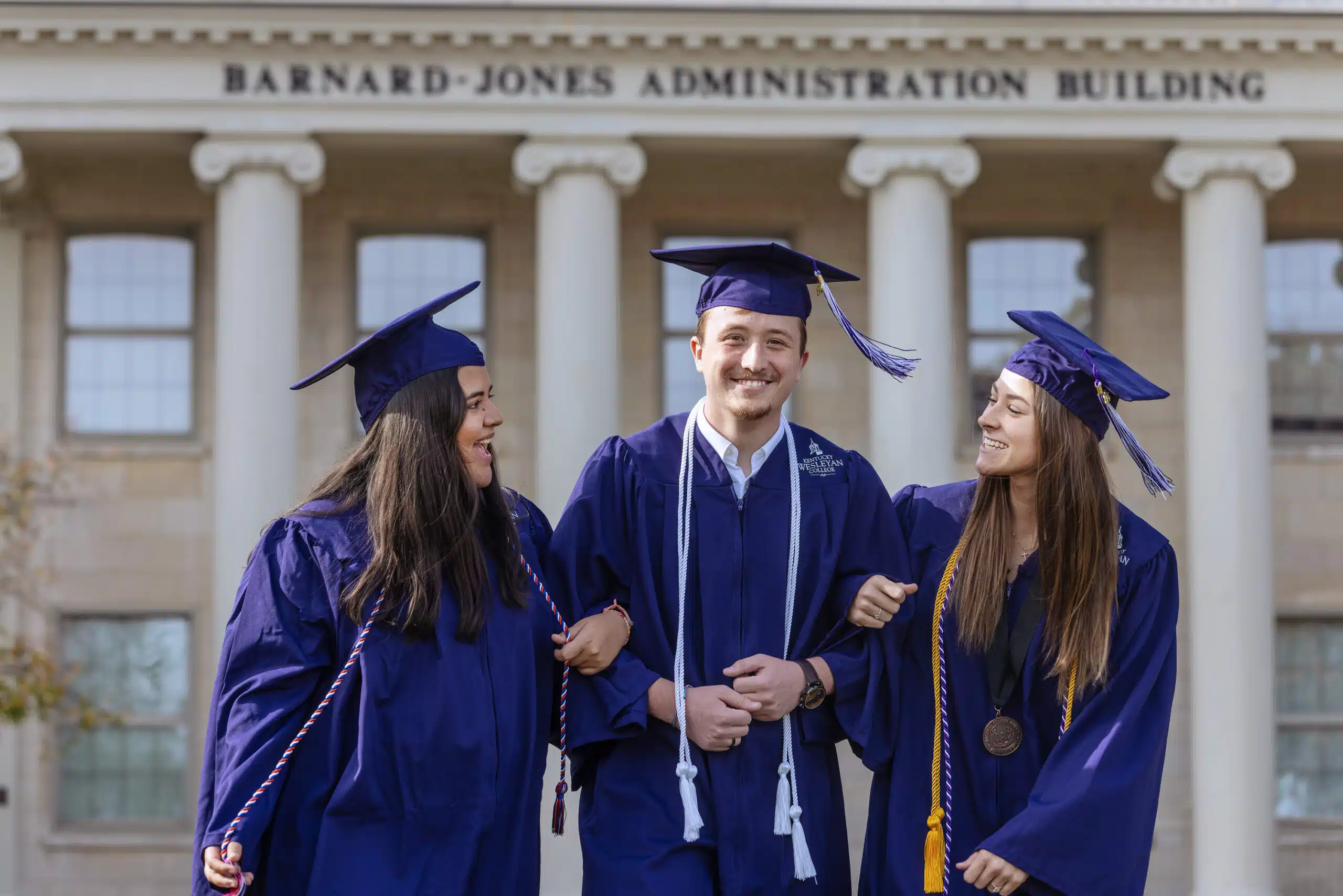 Three students in KWC caps and gowns outside the Administration Building