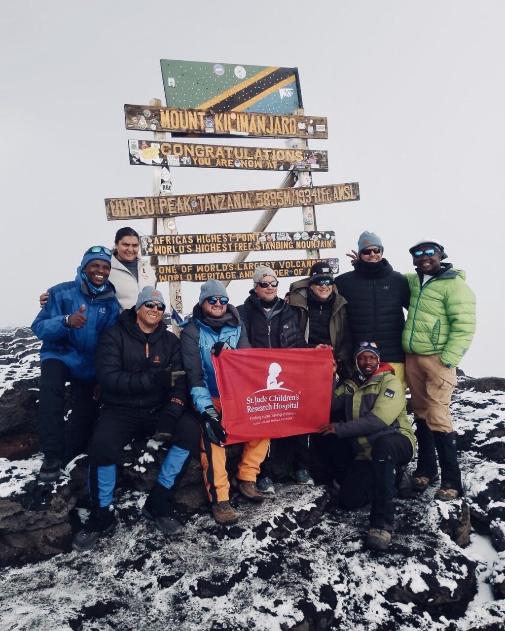 A group of hikers posing in front of the Mount Kilimanjaro post holding a St. Jude flag