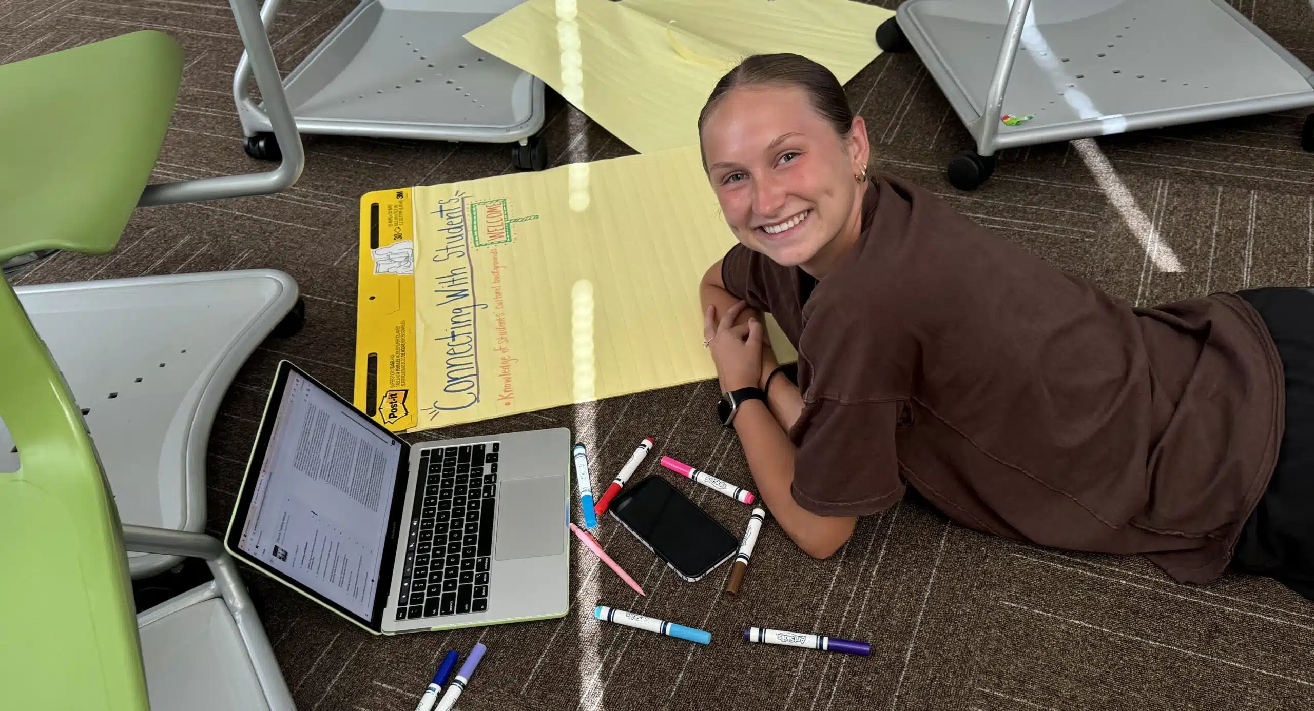 Student working on education project with markers, chart, and laptop