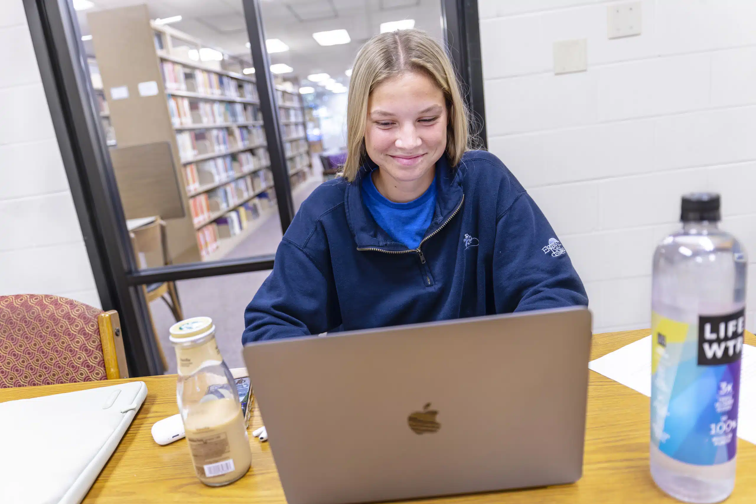 A student smiling and working on their laptop inside the KWC library