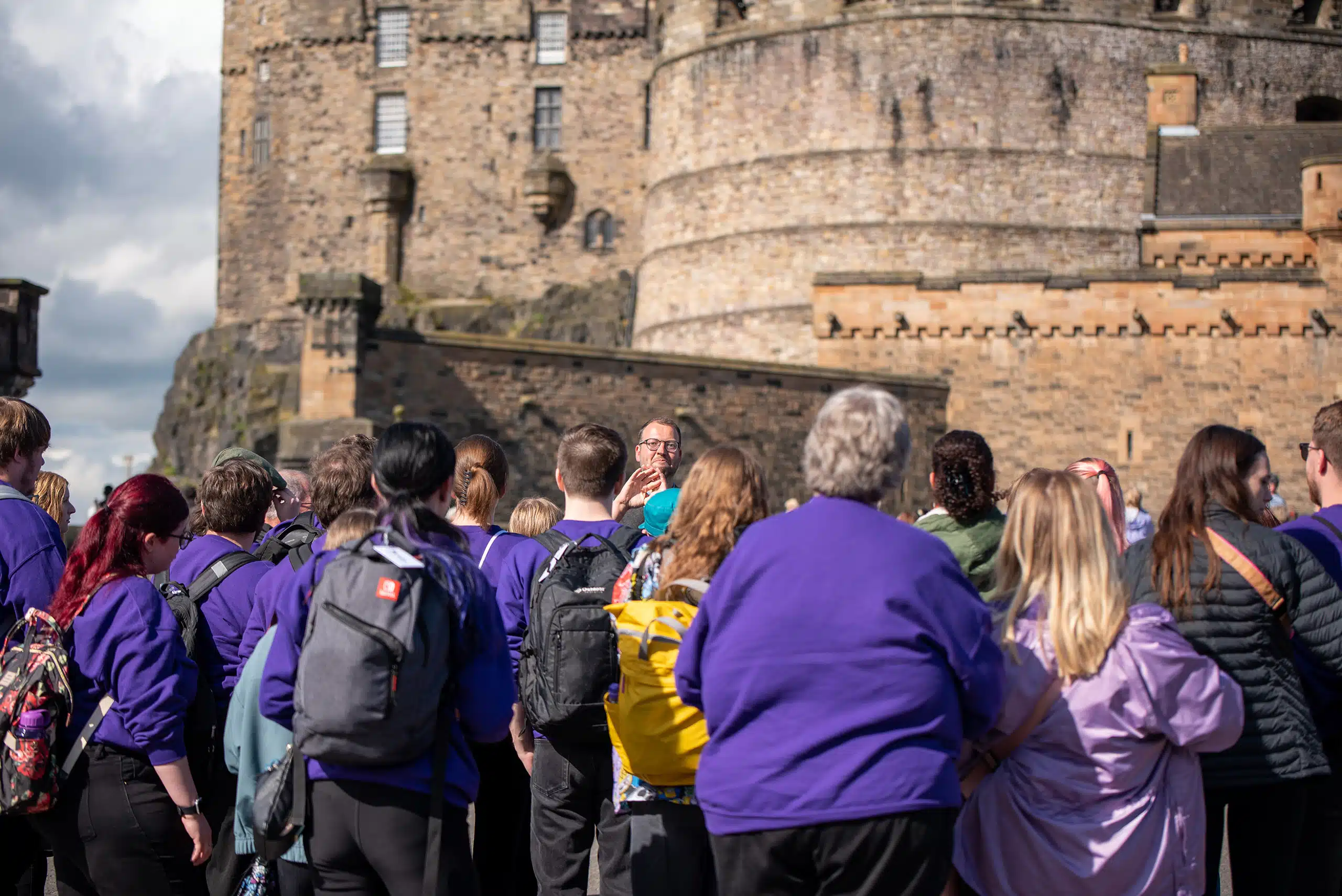 Choir students listening to tour guide in front of Scottish castle