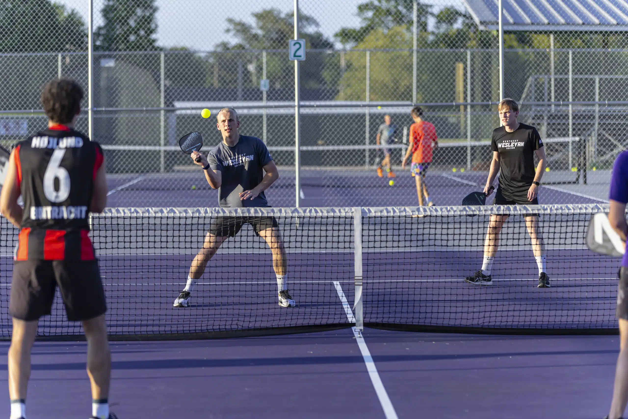 A group of students engaged in a game of pickleball on campus