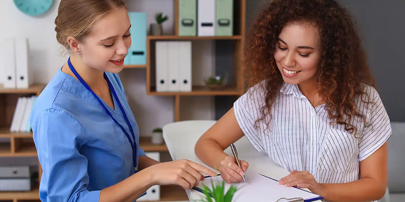 Medical administrative assistant helping a patient complete paperwork at a front desk