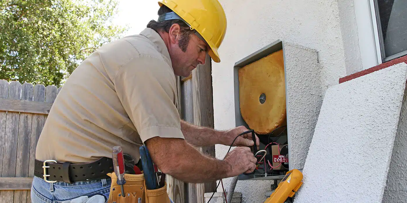 HVAC technician in a hard hat testing wiring on an outdoor unit