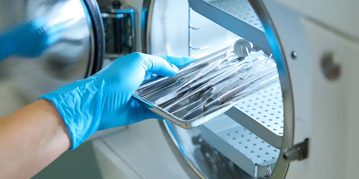 Gloved hand placing a tray of surgical instruments into a sterilizer